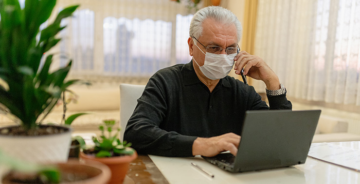 older man wearing a mask, using a laptop.