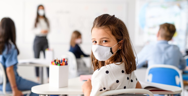 child at a school desk with mask on.
