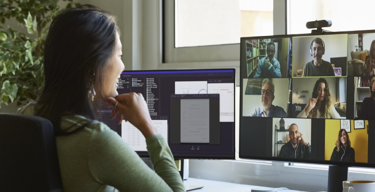 A person looking at a screen with a video call with many small tiles with people attending a meeting.