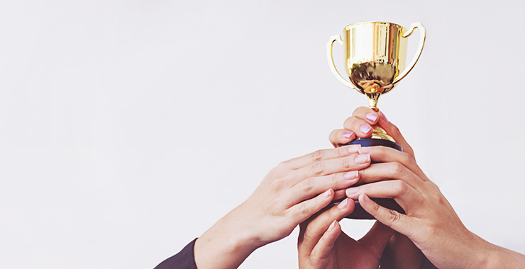 Several hands holding award cup aloft