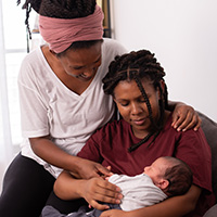 two women of color holding a baby