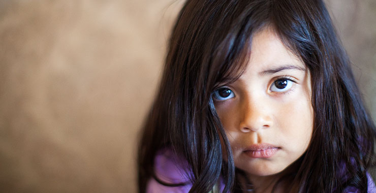 A small child with brown eye and dark hair is frowning.
