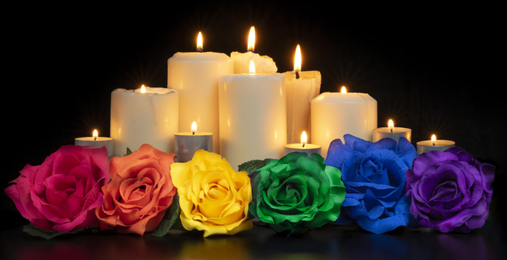 Candles and roses in a row that are in the color of a rainbow